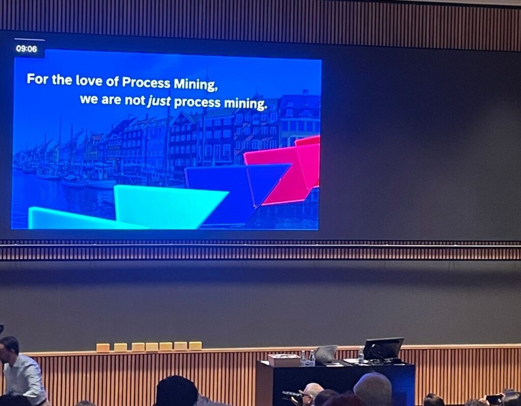 Stage view of a process mining presentation at ICPM 2024, with a speaker discussing advancements in AI-driven process mining, and an audience of attendees in a conference setting.